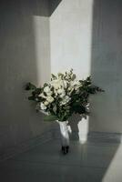 Gentle wedding bouquet of white roses and greenery, on a white background, sun rays and shadow. Wedding accessories.. photo