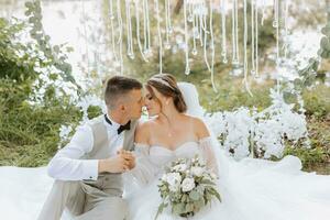 Groom and bride on their wedding day sitting holding hands outdoors. People are happy and smile. Happy couple in love looking at each other photo