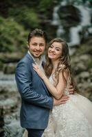 Portrait of a happy bride and groom near a waterfall. Bride and groom. Wedding photo session in nature. Photo session in the forest of the bride and groom.