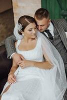 the bride and groom are sitting on a sofa against the background of green windows. Stylish bride and groom. Wedding photo. easy atmosphere photo