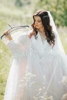 A beautiful bride with long curly hair holds her delicate dress and admires it in the garden. Morning of the bride. Natural makeup photo