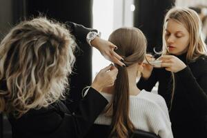 The face of a beautiful young woman. The process of creating hair and makeup. Beautiful hands in the process of work. White and black clothes. Three women with blond hair photo