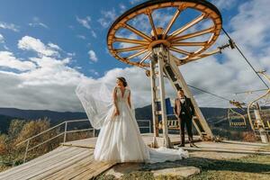 Married couple among mountains, bride looking back to groom, girl smiling, woman in white wedding dress, groom and brown suit photo