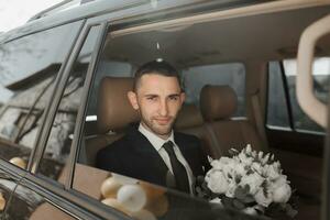 un elegante acicalar, preparando para el Boda ceremonia, se sienta en un coche. del novio Mañana. empresario vistiendo un chaqueta, masculino manos de cerca, novio consiguiendo Listo en el Mañana antes de el Boda ceremonia foto