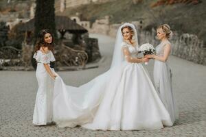 Stylish bridesmaids have fun with the bride in nature and pose to help the bride with the train of the dress photo