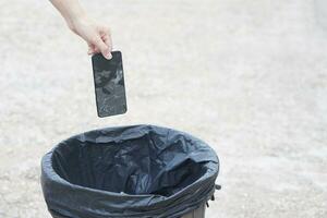 Closeup hand throw broken smartphone into the bin.Concept, hazardous electronic waste should sort before throwing for safety with environment. Technological garbage management. photo