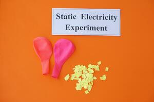 Ballons and small pieces of paper. Equipment, prepared to do experiment about static electricity. Orange background.  Concept, Science lesson, fun and easy experiment. Education. Teaching aids. photo