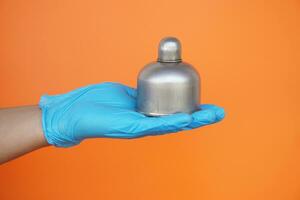 Close up  hands wears blue gloves hold alcohol burner  which used in laboratory , isolated on orange background. Concept, tool for doing science experiment. photo