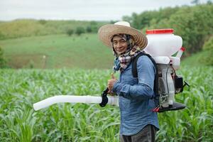 Asian man farmer carry fertilizer sprayer machine on back, stand at garden. Concept, farmer use engine facilitator tool in agriculture. Easy and fast for sowing. photo