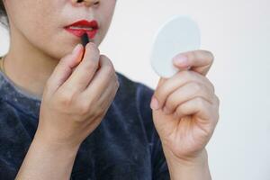 cerca arriba asiático mujer es aplicando rojo lápiz labial en su labios, Mira a pequeño espejo. concepto, mujer ama belleza. maquillaje y cosmético. feminidad. foto