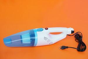 Portable electric vacuum cleaner on orange background. Concept, Household electric appliance device for cleaning. Get rid of dust or scraps. photo