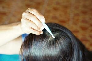 Close up senior woman hand holding tweezers to pluck gray hair from head. Concept, health care. Get rid of gray hair. photo