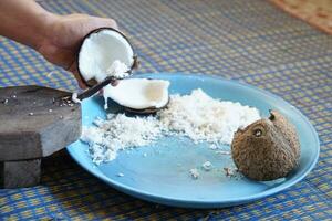 Hands  holding a half-cut coconut to scrape for making coconut milk by using coconut grater. Concept Thai cooking style. photo