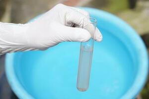 Close up ecologist hand wears glove holds test tube of water. Concept, Inspecting water quality from nature source that use in daily life. Examination water pollution. Environmental problems. photo