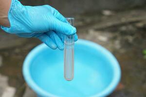 Close up ecologist hand wears glove holds test tube of water. Concept, Inspecting water quality from nature source that use in daily life. Examination water pollution. Environmental problems. photo