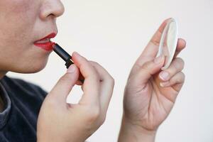 Close up Asian woman is applying red lipstick on her lips, look at small mirror. Concept, Woman loves beauty. Makeup and cosmetic. Femininity. photo