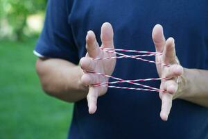 Closeup man hands is playing rope which called cats cradle game. Concept, game involving the creation of various style figures between the fingers. Traditonal playing. photo