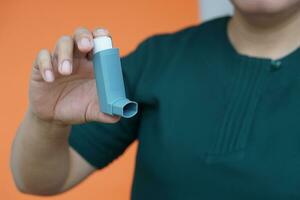 Close up patient's hand holds asthma inhaler. Concept, health care. Pharmaceutical products for treatment symptoms of asthma or COPD. Use under prescription. Health care device at home. photo