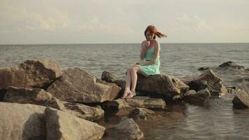 global planifier. magnifique sexy fille dans une bérusien robe avec rouge cheveux séance sur des pierres à le mer video