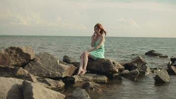 Overall plan. Beautiful sexy girl in a birch dress with red hair posing on rocks at the sea video