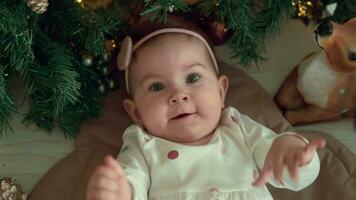 Happy 1 year old child lies near the Christmas tree and laughs. video