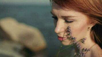 portrait. lent mouvement. magnifique content sexy fille avec longue rouge cheveux dans une robe est assis sur le mer Contexte avec une bien ambiance video