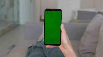 femme tapoter sur le centre de une vert écran téléphone tandis que mensonge sur le canapé à maison. Cliquez sur sur le centre de le filtrer. video