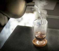 Shot of the hot water being poured into the transparent cup to brew the coffee. Beverage photo