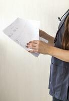 Shot of the female doctor in uniform against the white wall studying cardiogram. Healthcare photo