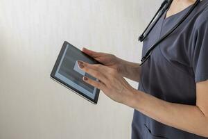 Shot of the female doctor in uniform against the white wall studying x-ray image of the lungs on the tablet. Healthcare photo