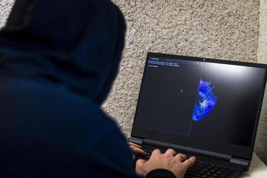 Man looked like hacker in a hood sitting in the front of laptop, writing a code. Cyber security photo