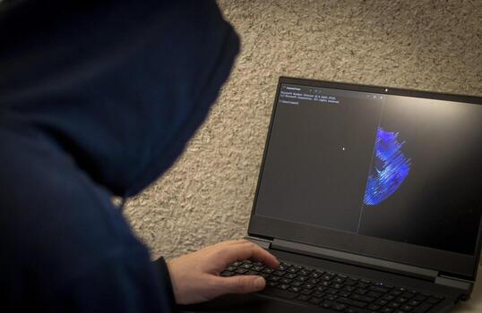 Man looked like hacker in a hood sitting in the front of laptop, writing a code. Cyber security photo