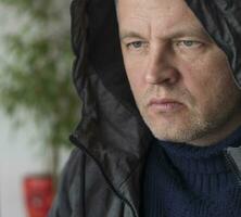 Portrait of the mid aged man with grey hair, wearing warm, dark blue sweater and grey coat. People photo