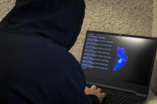 Man looked like hacker in a hood sitting in the front of laptop, writing a code. Cyber security photo