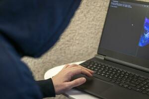 Man looked like hacker in a hood sitting in the front of laptop, writing a code. Cyber security photo