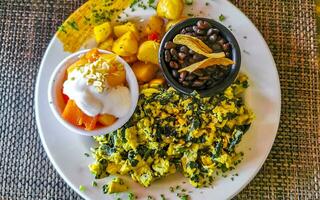 Breakfast scrambled eggs spinach fruit potatoes nicely arranged on plate. photo