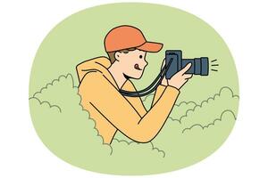 Young man reporter hide in bushes make pictures vector