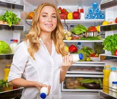 Woman chosen yogurt in opened refrigerator photo