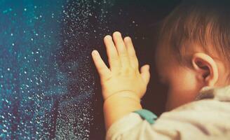Baby looking through rainy window photo