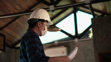 professioneel Azië ingenieur vervelend helm en Holding de verslag doen van controleren detail dak structuur in huis bouw plaats werk. video