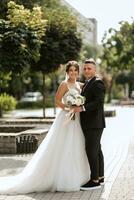 el novio con traje marrón y la novia con vestido blanco foto