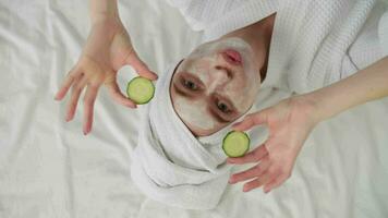 Skin Care, After Bath, Cosmetics at Home, Caucasian Woman, Anti Aging. Caucasian woman in bathrobe after bath fooling around lying on bed and using cosmetic face mask with cucumber video