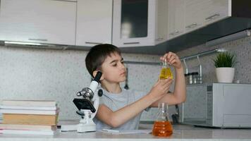 Attractive Boy teaches chemistry using a microscope and flasks with liquid and makes notes in a notebook. Homework. video