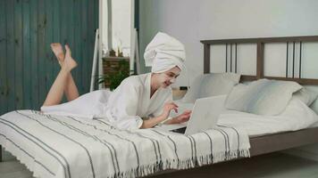 Skin Care, After Bath, Cosmetics at Home, Online Meeting, Distance Learning. Caucasian woman in a robe and a towel on her head uses a laptop. Cosmetic mask on the face video