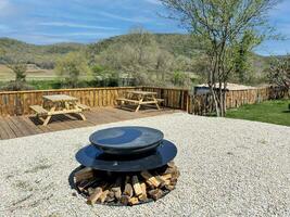 Camping site with fire pit and woods, wooden desks on a deck and natural mountain view in the background. photo