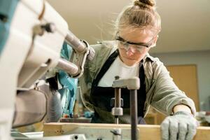 Female Carpenter Wearing Protective Safety Glasses and Using Electric Work on a Wood. Artist or Furniture Designer Working on a Product Idea in a Workshop. photo