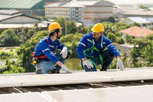 Men technicians carrying photovoltaic solar modules on the factory roof. Engineers in helmets installing solar panel systems outdoors. Concept of alternative and renewable energy. photo