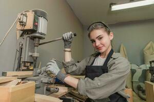 hembra carpintero vistiendo protector la seguridad lentes y utilizando eléctrico trabajo en un madera. artista o mueble diseñador trabajando en un producto idea en un taller. foto