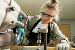 Female Carpenter Wearing Protective Safety Glasses and Using Electric Work on a Wood. Artist or Furniture Designer Working on a Product Idea in a Workshop. photo