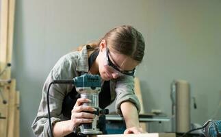 Female Carpenter Wearing Protective Safety Glasses and Using Electric Work on a Wood. Artist or Furniture Designer Working on a Product Idea in a Workshop. photo
